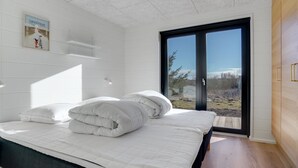 Een moderne slaapkamer met een groot bed, een glazen schuifdeur naar een balkon en uitzicht op de omgeving.