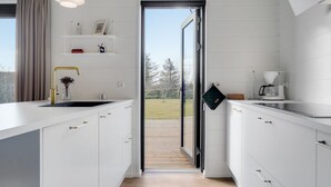 Een moderne keuken met witte kastjes, een gouden kraan en zicht door een geopende deur op een houten terras.