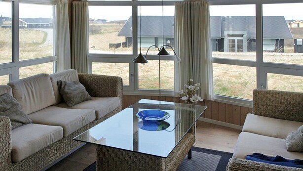 Un salon moderne avec une table basse en verre, des meubles en osier et de grandes fenêtres donnant sur la campagne.