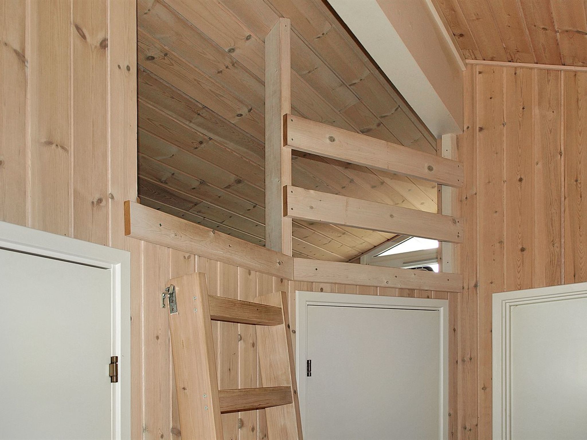 Un intérieur en bois avec un plafond incliné, des murs en bois et des portes blanches.