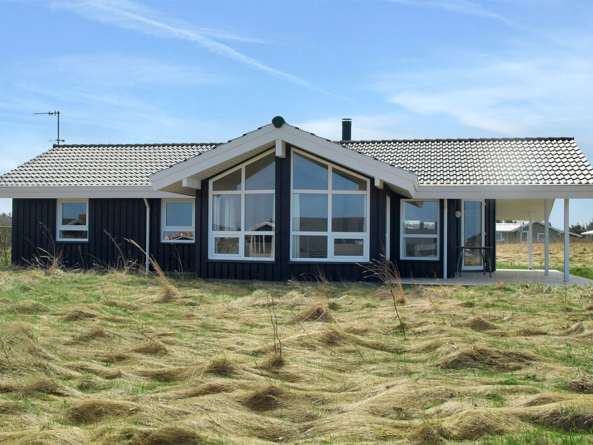 Une maison moderne dotée d’une grande fenêtre à l’avant, d’un porche couvert et d’un toit en pente.