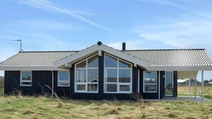 Une maison moderne dotée d’une grande fenêtre à l’avant, d’un porche couvert et d’un toit en pente.