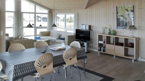 Un espace de vie moderne, à aire ouverte, comprenant un coin repas, des sièges, un téléviseur et une bibliothèque.