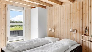 A bedroom with a wooden ceiling, a bed with white bedding, a window with a view of greenery, and two wall-mounted lamps. - "Ellen" - 289m from the sea by Interhome (Hjørring)
