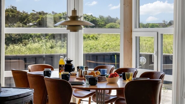 A dining area with a table set for four, large windows, and a hanging pendant light. - "Ellen" - 289m from the sea by Interhome (Hjørring)