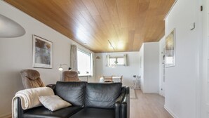 Ein modernes Wohnzimmer mit einer schwarzen Ledersofa, einer Holzbalkendecke und einem Essbereich mit Tisch und Stühlen.