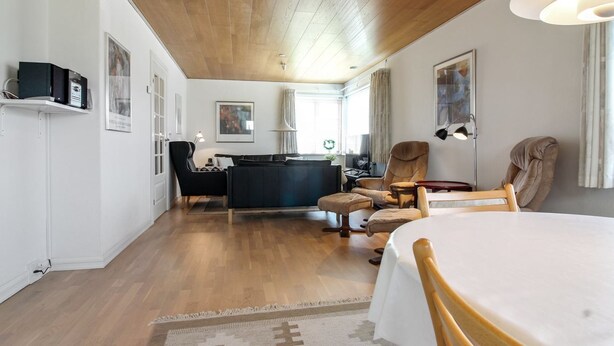 Ein modernes Wohnzimmer mit Holzboden, einer Couch, einem Esstisch und einem Fernseher auf einem Regal.