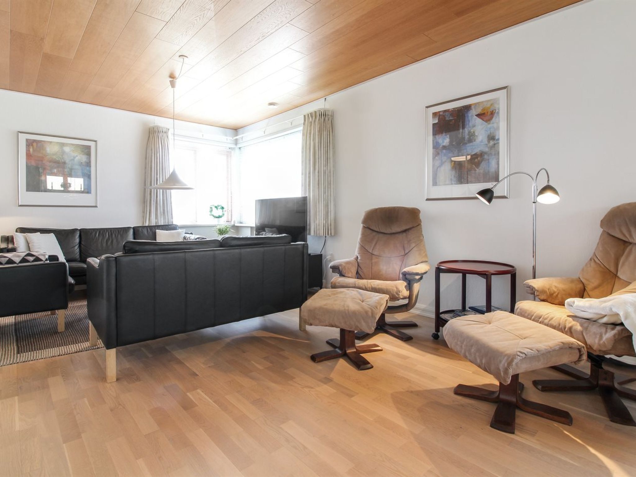 Un salon moderne avec un canapé noir, des fauteuils beiges et un parquet.