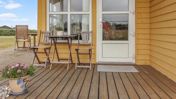 Eine Holzterrasse mit Tisch und Stühlen, einem Blumentopf und einer Tür mit Fenster.