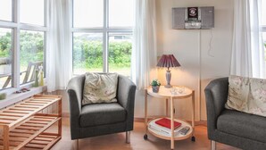Ein Zimmer mit zwei grauen Sesseln, einer Holzablage, einem kleinen Tisch mit Lampe und einem Radio an der Wand.