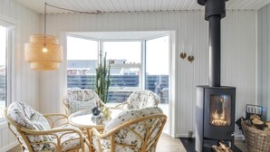 Una habitación acogedora con una mesa redonda y sillas de mimbre, un estufa de leña negra y un ventanal con vistas a edificios.