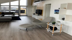 Un salon moderne comprenant un canapé, un fauteuil et une table basse, ainsi qu’une télévision et une bibliothèque.