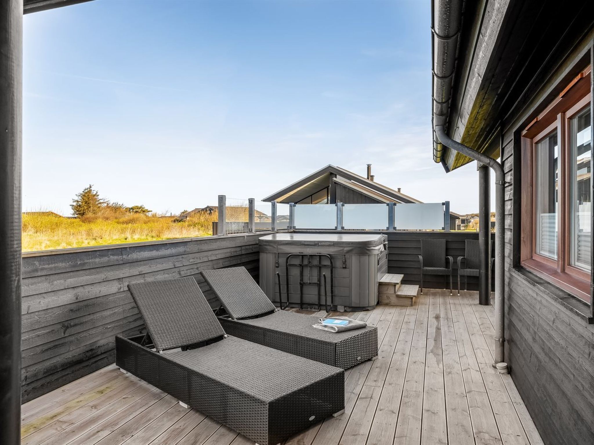 Una terraza de madera con un jacuzzi, sillones de descanso y vistas al paisaje.