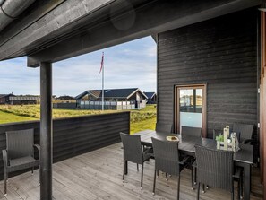 Et overdækket udendørs område med et bord og stole samt udsigt til huse i baggrunden og en flagstang.