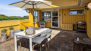 Edifício amarelo com um pátio que inclui mesa, cadeiras e guarda-sol.