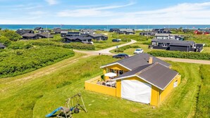 Uma área residencial costeira com casas, um campo gramado e vista para o mar.