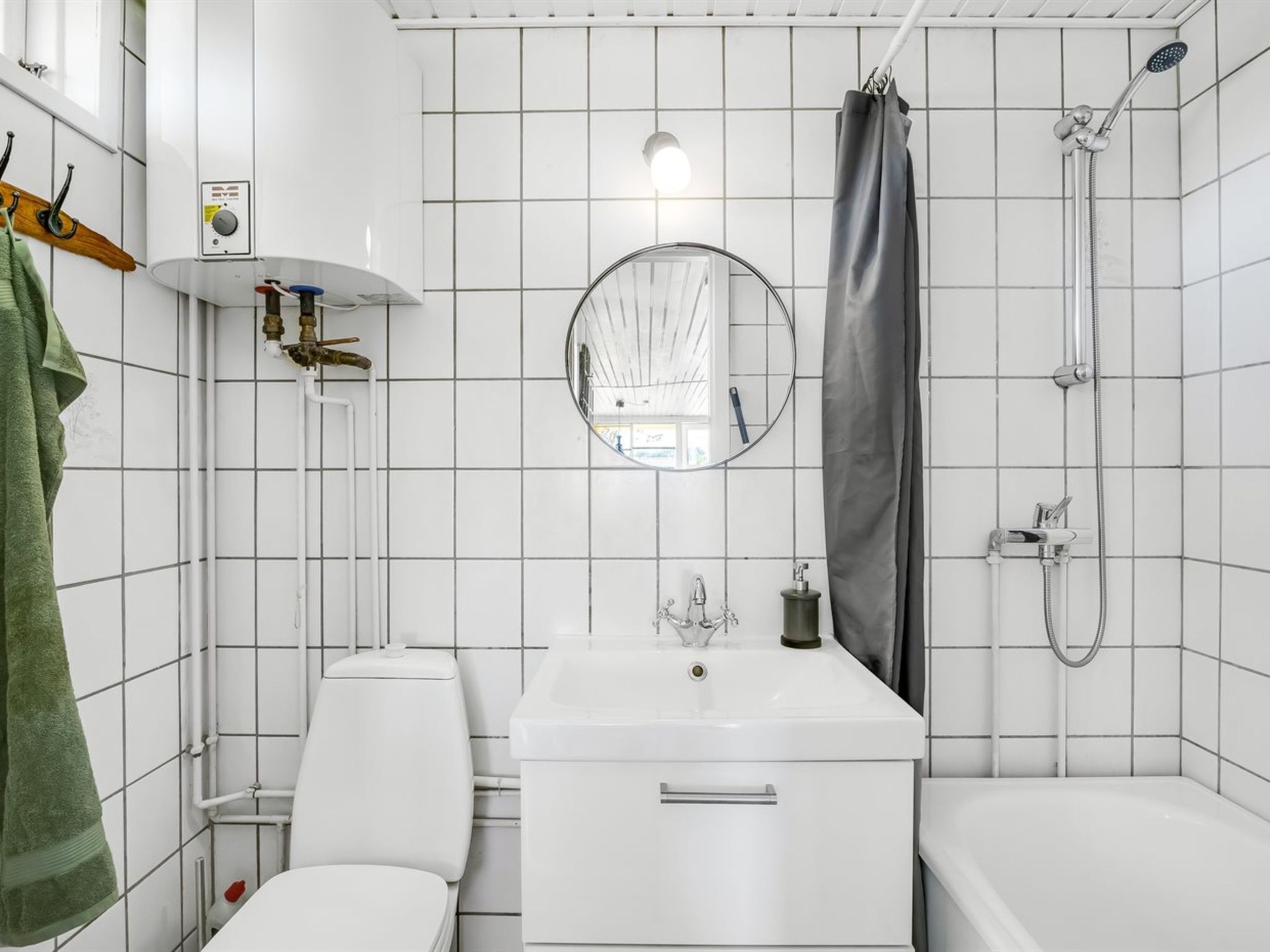 Et badeværelse med toilet, vask, spejl, bruser og håndklædetørrestativ.