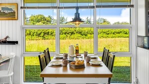 Uma sala de jantar com uma mesa posta para quatro pessoas, janelas amplas e um lustre.