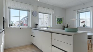 A modern kitchen with white cabinetry, a large island, a clock, and a window with a view of a building outside.