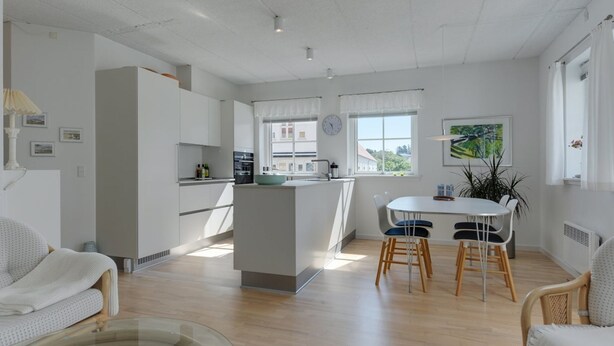 A modern kitchen with white cabinets, a central island, and a dining area with a white table and chairs.
