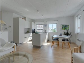 Een moderne keuken met witte kasten, een centraal eiland en een eethoek met een witte tafel en stoelen.