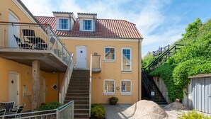 A yellow building with a red-tiled roof, a staircase, and a small garden area.