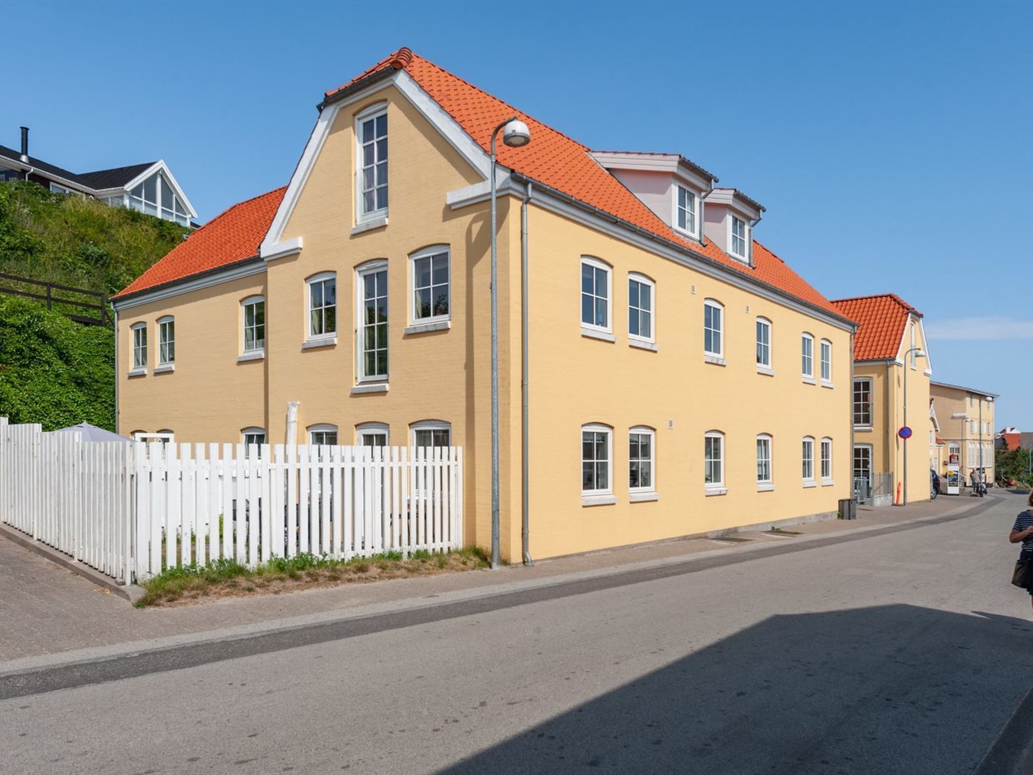 Keltainen rakennus, jossa on punainen katto, valkoiset ikkunat ja valkoinen koristelista-aita.