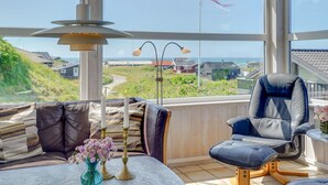 Ein Zimmer mit Blick auf ein Küstendorf, ein Tisch mit Blumen in einer Vase, ein blauer Stuhl und eine Lampe.