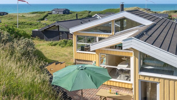 Ein Küstenhaus mit Terrasse, einem grünen Sonnenschirm und Meerblick.