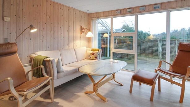A modern living room with a wooden wall, a white sofa, a glass coffee table, and two brown leather chairs. - "Liisi" - 500m from the sea by Interhome (Hjørring)