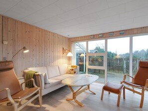 Een moderne woonkamer met een houten wand, een witte bank, een glazen salontafel en twee bruine leren fauteuils.