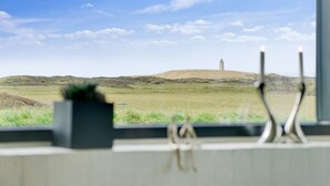 Vista des d'una finestra sobre un camp verd amb un turó i una torre a la distància.