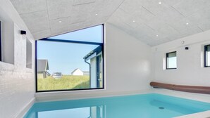 Una piscina coberta moderna amb un gran finestral que ofereix vista a un camp de gespa i una casa.