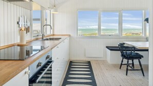 Eine moderne Küche mit einem großen Fenster, einer Holz Arbeitsplatte und Blick aufs Meer.