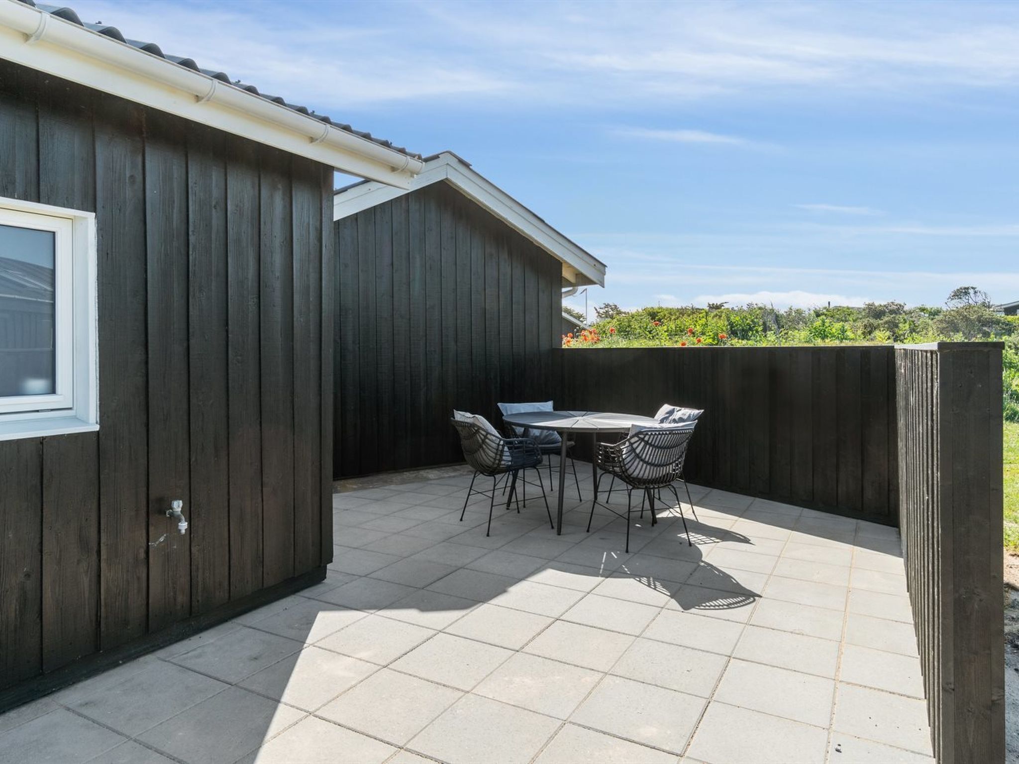 Un patio con tavolo e sedie, una finestra e una recinzione in legno.