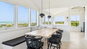 Ein Essbereich mit einem Holztisch und schwarzen Stühlen, großen Fenstern mit Meerblick und Pendelleuchten.
