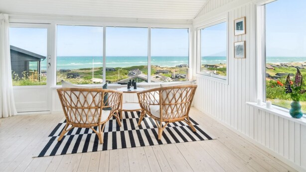 Ein Zimmer mit großem Fenster mit Blick auf einen Strand, einem Schachbrettteppich und Korbstühlen.