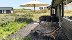 Une terrasse dotée de mobilier d’extérieur, comprenant une table et des chaises, ainsi qu’un grand parasol.