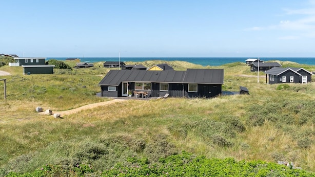 Une zone côtière où se trouvent de nombreuses petites maisons, dont certaines sont dotées de vérandas, le tout sur fond de dunes et de mer.