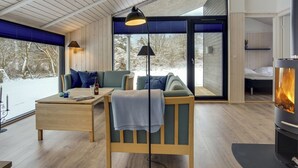A cozy cabin interior with a wooden floor, a sofa, a table, and a fireplace.