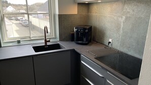 Eine moderne Küche mit integriertem Spülbecken, einer Kaffeemaschine und einem Fenster mit Blick auf einen Parkplatz.