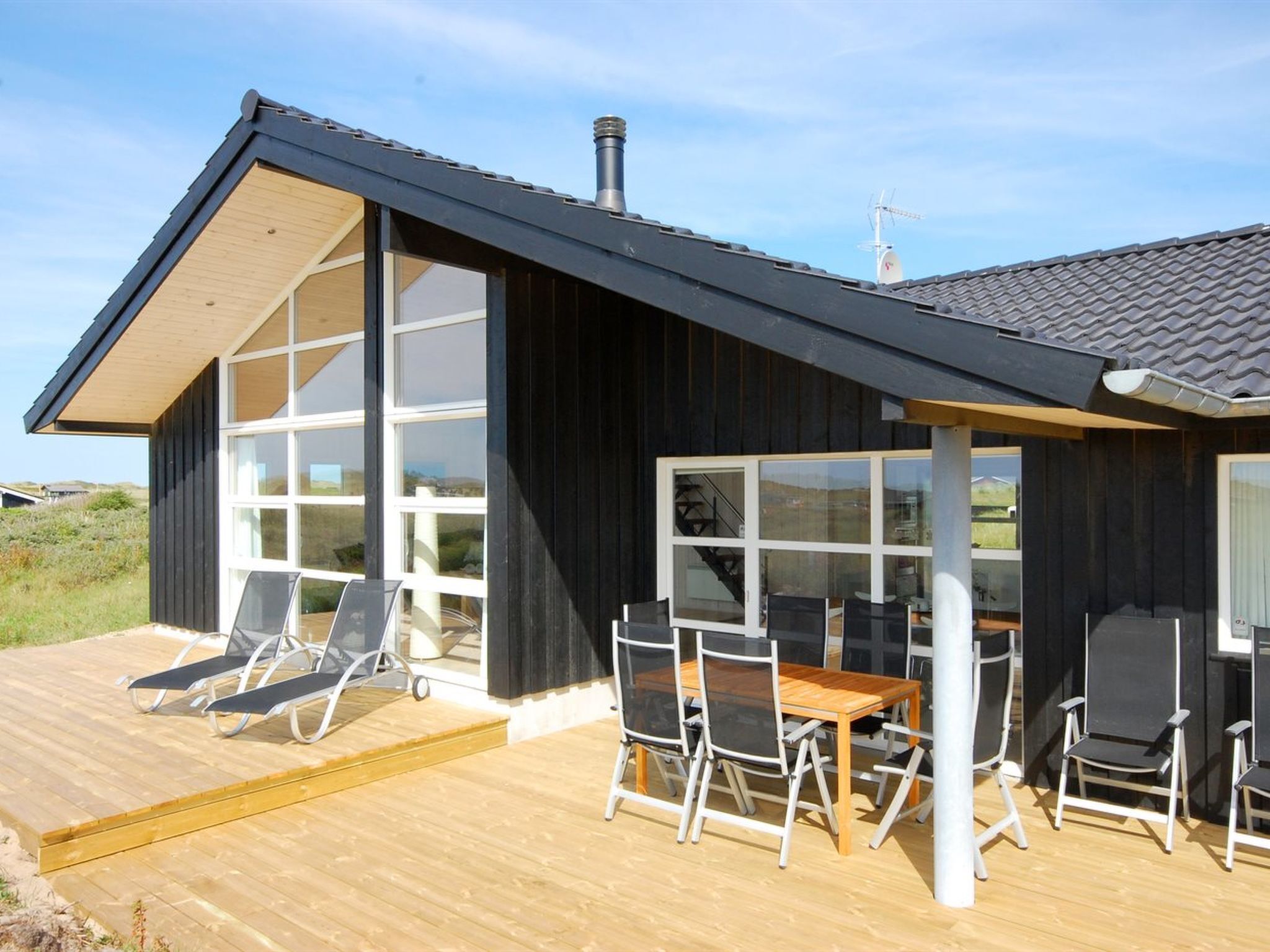 En moderne bygning med store vinduer og en træterrasse med udendørs siddepladser.