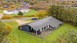 Une maison moderne dotée d’une grande terrasse, entourée d’une pelouse bien entretenue et d’arbres.