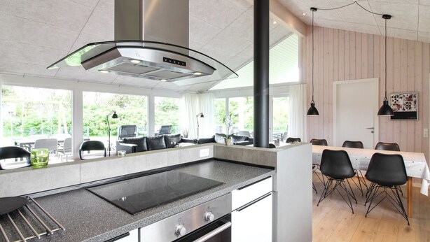 Une cuisine moderne dotée d’un grand îlot central, d’appareils électroménagers en acier inoxydable et d’un coin repas avec une table et des chaises en bois.