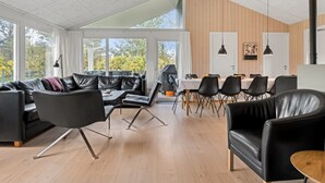 Un vaste espace de vie comprenant un grand canapé en cuir noir, une table à manger avec des chaises et un plancher en bois.