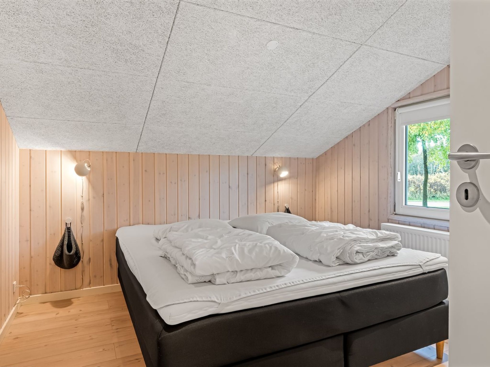 Quarto com cama, paredes de madeira, janela e radiador.