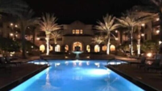 A swimming pool with a fountain at the center, surrounded by palm trees and a building with multiple windows in the background. - Bohemian Rhapsody King Suite St. Augustine at WGV (St. Augustine)