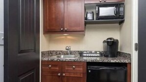 A compact kitchen with dark wooden cabinets, a microwave, a coffee maker, and a dishwasher. - Bohemian Rhapsody King Suite St. Augustine at WGV (St. Augustine)