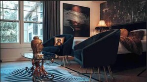 A modern bedroom with a large window, a zebra-patterned rug, a bed, a chair, and a small table. - Bohemian Rhapsody King Suite St. Augustine at WGV (St. Augustine)