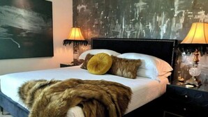 A bedroom with a large bed, two bedside lamps, a fur throw, and a cityscape mural on the wall. - Bohemian Rhapsody King Suite St. Augustine at WGV (St. Augustine)